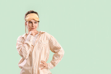 Thoughtful young woman in pajamas on green background
