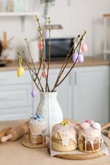 Vase with tree branches and tasty Easter cakes on dining table in kitchen
