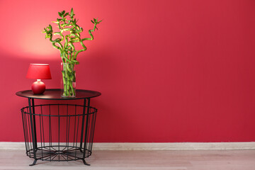 Vase with bamboo branches and lamp on table near color wall