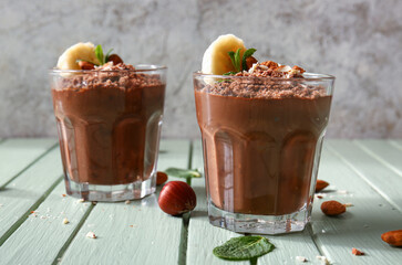 Glasses of delicious chocolate pudding with almond, banana and mint on green wooden table