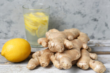 Fresh ginger roots, glass of water and lemon on wooden table