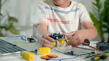 Asian kid boy assembling wheel into Arduino robot car homework, Little child trying assemble build wheel to car toy, creating electronic AI technology workshop online school lesson