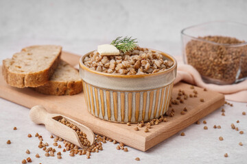 Bowl of tasty buckwheat porridge with butter, dill and scoop of grains on grey table