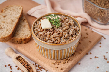 Bowl of tasty buckwheat porridge with butter, dill and scoop of grains on grey table