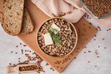Bowl of tasty buckwheat porridge with butter, dill and scoop of grains on grey table
