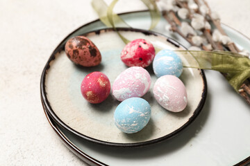 Plate with painted Easter eggs and willow branches on light background, closeup