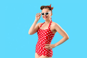 Young pin-up woman in polka dot swimsuit on blue background