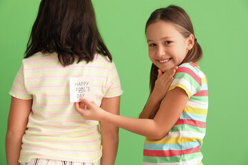 Little girl playing a prank on her sister against green background. April Fools' Day celebration