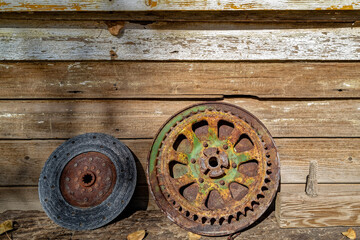 Fototapeta na wymiar A rusty gear and brake rotor leaning against the wall of an old wood building