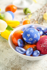 Bowl with painted Easter eggs and candies on light table, closeup