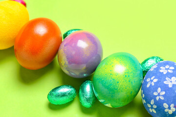 Composition with painted Easter eggs and candies on green background, closeup