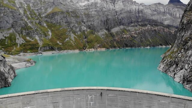 Aerial view of turquoise waters of lake Limmernsee and hydroelectric dam in Linthal Glarus, Switzerland with cliffs in background