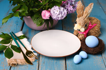 Table serving with Easter eggs, bunny and floral decor on blue wooden background