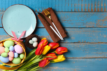 Table serving with tulip flowers and basket of Easter eggs on blue wooden background