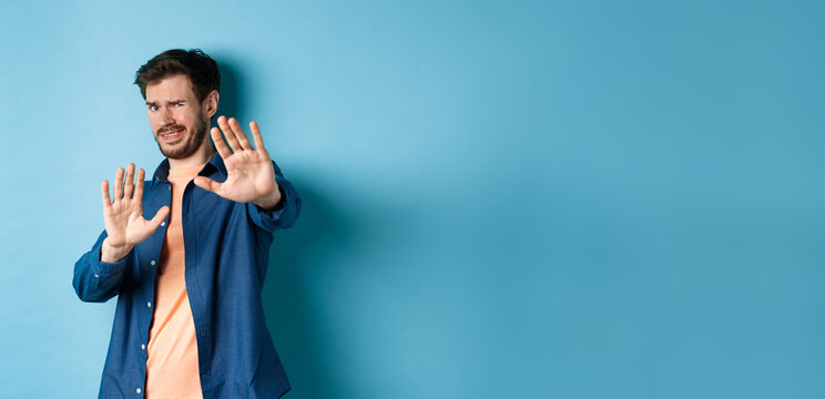 Guy Cringe From Something Disgusting Or Embarrasssing, Stretching Out Hands And Asking To Stop, Grimacing Displeased, Standing On Blue Background