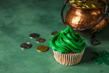 Tasty cupcake for St. Patrick's Day and pot of coins on green background