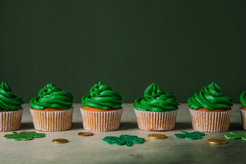 Fototapeta na wymiar Tasty cupcakes for St. Patrick's Day, clovers and coins on grunge table against green background