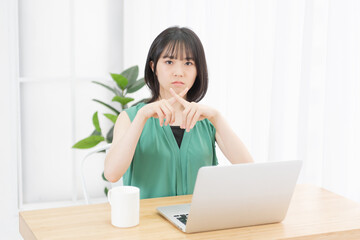 PCの前でNGのサインを見せる若い女性