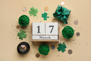 Tasty cupcakes for St. Patrick's Day, cube calendar with date MARCH 17, coins and clovers on beige...
