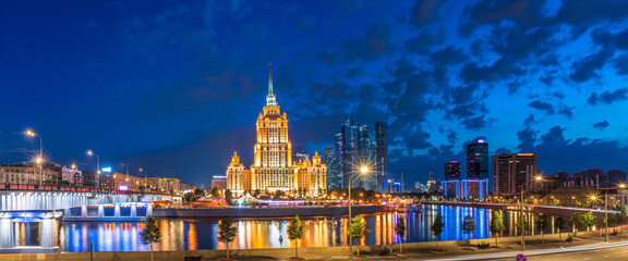 Illuminated high-rise stalinist building near river at summer night in Moscow, Russia. Historic name is Hotel Ukraina. - obrazy, fototapety, plakaty