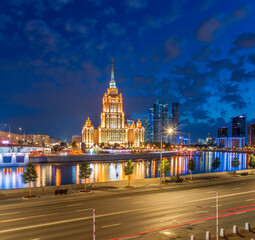 Illuminated high-rise stalinist building near river at summer night in Moscow, Russia. Historic...