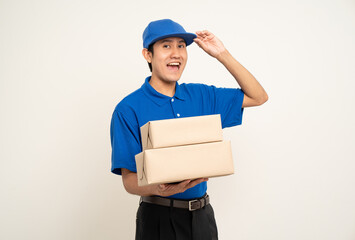 Happy delivery asian man in blue uniform standing holding box parcel cardboard on isolated white background. Smiling male service worker. Delivery courier and shipping service.