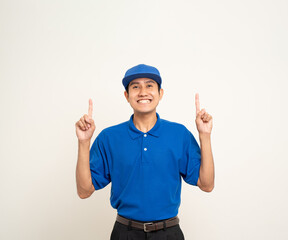 Happy asian man in blue uniform standing on isolated white background. Smiling male delivery service worker pointing the finger to blank space. Delivery courier and shipping service.