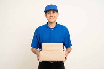 Happy delivery asian man in blue uniform standing holding box parcel cardboard on isolated white background. Smiling male service worker. Delivery courier and shipping service.