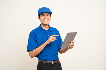 Asian man in blue uniform standing holding digital tablet computer on isolated white background. Male service worker with cell phone. Delivery courier shipping service