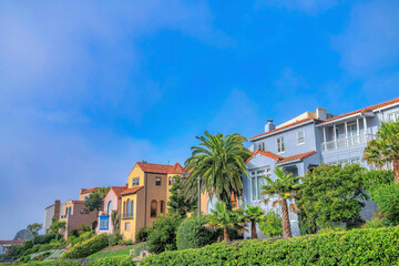 Fototapeta na wymiar Residential landscape with colorful houses in San Francisco Califronia. Facade of homes in a beautiful neighborhood with vibrant foliage against blue sky.