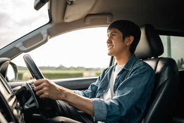 A young Asian man drives a car on a clear day. With beautiful blue sky. He smiling driving to...
