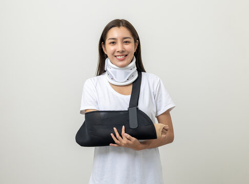 Happy young asian woman broken arm on isolated background. Asian female put on plaster bandage cast splint. Patient wearing sling support arm after accident injury. life insurance and accident