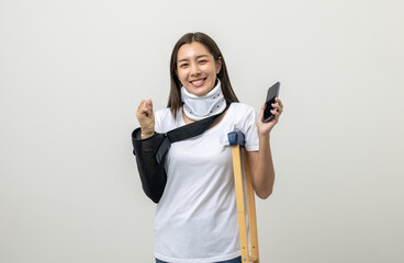 Happy young asian woman broken arm holding smartphone. Woman put on plaster cast splint with...