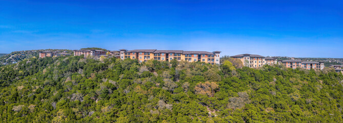 Fototapeta premium Apartment complex on a mountain top with green trees against the blue sky in Austin, Texas. Panorama of a multi-storey apartment buildings.