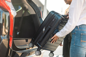 Happy couple puts his suitcase in the back of the car and prepares to leave for honeymoon trip....