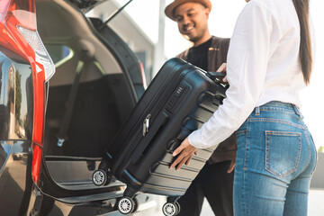 Happy couple puts his suitcase in the back of the car and prepares to leave for honeymoon trip....