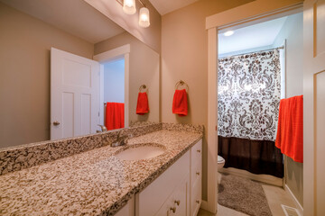 Utah- Bathroom with separate room for toilet and bathtub. There is a vanity sink with granite counter and mirror beside the room with toilet and tub with curtain near the hanging red orange towels.