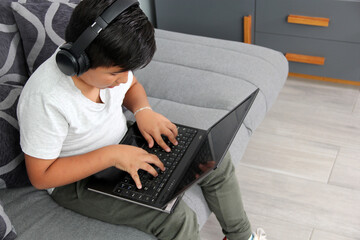9-year-old Hispanic boy plays video games on his laptop with headphones leading to being overweight and poor sitting posture - obrazy, fototapety, plakaty