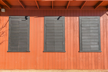 Vertical wood wall cladding with three closed painted wooden window cover at Austin, Texas. Painted gray side hinged wooden windows close-up.