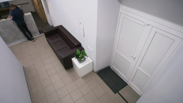 Client stands on reception at hall, talks with female secretary and discuss information displayed on phone. Adult man walks at corridor. Waiting at lobby in business center. Security camera shooting.