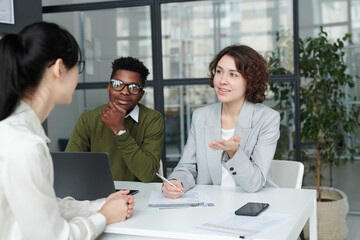 Young businesswoman together with her colleague asking questions to candidate during job interview