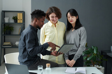 African American businessman pointing at digital tablet and showing presentation to his colleagues