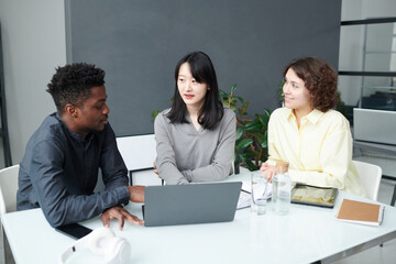 Group of colleagues discussing online project on laptop in team during business meeting in modern...