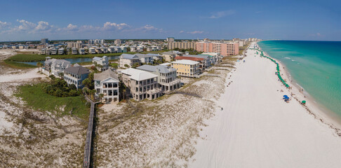 Multi storey buildings overlooking East Jetty and sunny beach in Destin Florida. Aerial view of a scenic coastal landscape with ocean, sandy shore, houses, and blue sky.