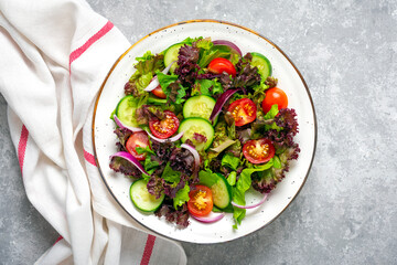 Healthy vegetable salad of cherry tomatoes, cucumber slices, green and purple lettuce leaves, onions and olive oil in plate on concrete table Top view Flat lay Diet, mediterranean menu Vegan food
