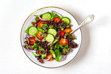 Healthy vegetable salad of red cherry tomatoes, cucumber slices, green and purple lettuce leaves, onions and olive oil in plate on white table Top view Flat lay Diet, mediterranean menu Vegan food