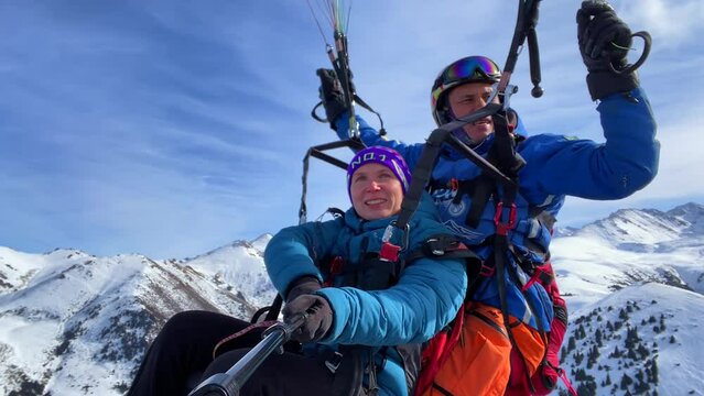 A girl with an instructor is paragliding over the Karakol mountain ski base, against the backdrop of majestic mountains and snow-white slopes covered with coniferous forests.