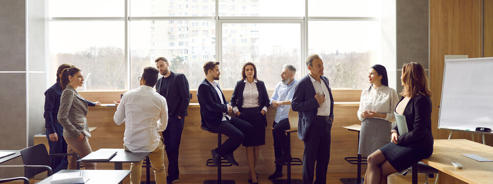Diverse groups of colleagues communicating with each other during break on business presentation in office meeting room. Business people discuss presentation, work, share thoughts and ideas. Panorama.