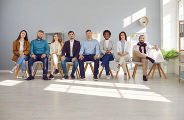 Human resource. Confident smiling multiracial professional business people of all ages sit on chairs in a row. Group portrait of happy job candidates looking at camera while sitting in light office