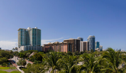 Beautiful Miamai Florida skyline with apartments against sunny blue sky. Lush green trees and roads can be seen in front of the modern residential buildings.